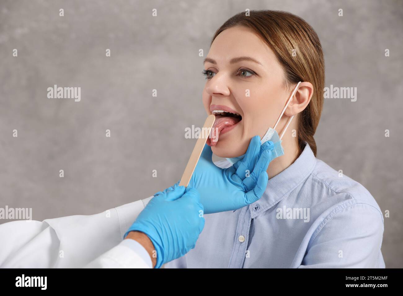 Doctor examining woman`s oral cavity with tongue depressor indoors